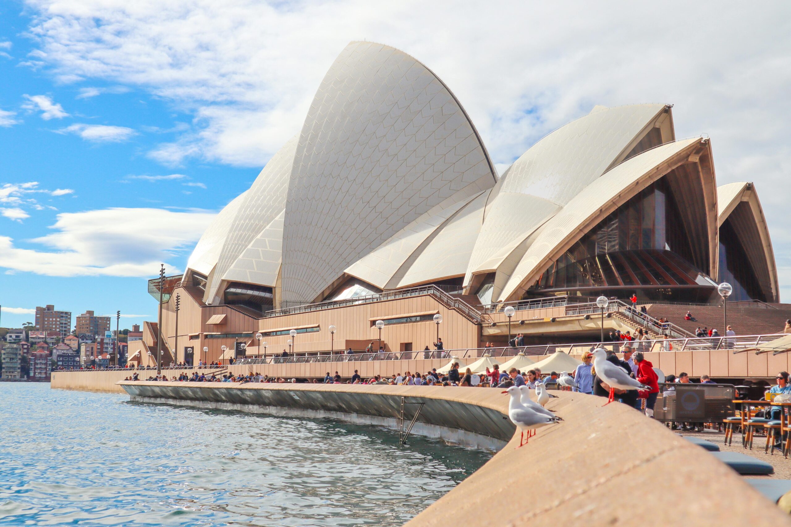 Sydney Opera House with tourists and waterfront view on a sunny day.